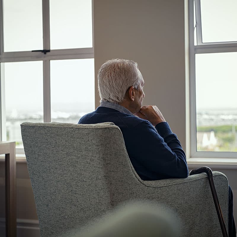 Old man in an armchair looking out of the window, pensive