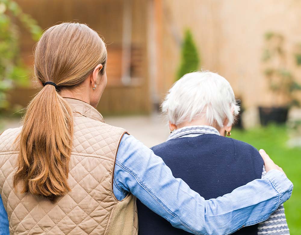 View from the back of elderly woman embraced by caretaker.